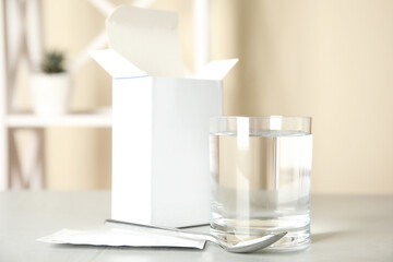 Medicine sachet, glass of water and spoon on light table