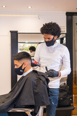 Young hairdresser with mask and gloves cutting hair. Security measures of Hairdressers in the Covid-19 pandemic, vertical photo