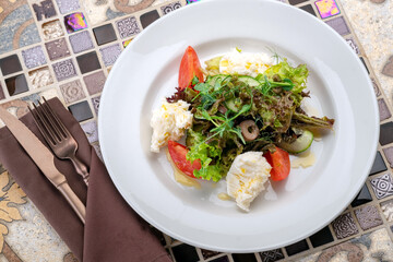Fresh green salad with goat cheese, arugula and olives on a white plate