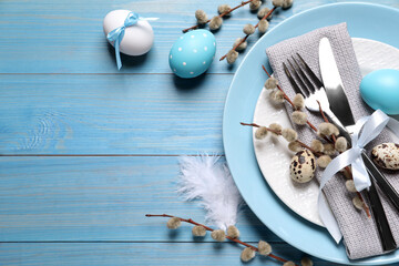 Festive Easter table setting with eggs on light blue wooden background, flat lay. Space for text