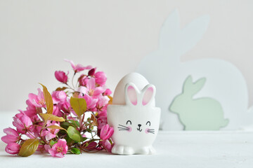Happy Easter holiday concept with cute bunny and fresh pink flowers on white table background. Greeting card. Easter background.