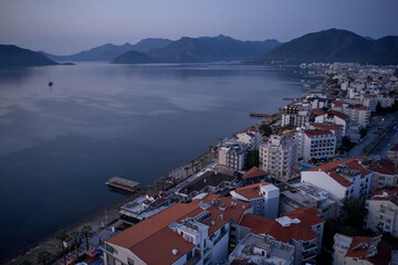 Aerial panoramic view of Marmaris city at sunset. Landscape view of resort town with sea, embankment, houses and mountains. Travel to Turkey.