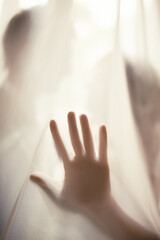 Silhouette of the palm of a human's hand with spread fingers under an organza on the background of...