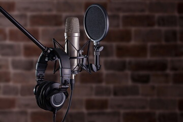 Studio condenser microphone with pop filter on stand with headphones on stone texture background