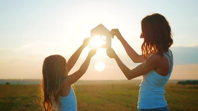 Silhouette happy mother and daughter with dream house. Paper house as a symbol. The concept of family happiness.