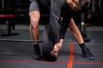 Sportsman adding weight to barbell changing black plates, equipment for weight training concept. Sports equipment for training. at modern gym alone