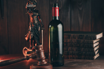 Bottle of wine and lady of justice on a wooden desk. Alcohol addiction.