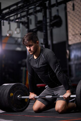 sportsman standing on his knee preparing to make deadlift at gym, young caucasian man in black sportswear engaged in bodybuilding, concentrated on weightlifting. sport, cross fit concept