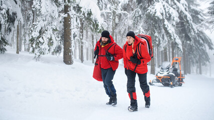 Paramedics from mountain rescue service walking outdoors in winter in forest.