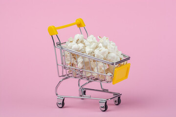 Shopping cart with popcorn on a pink background.