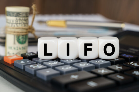 There are cubes on the calculator that say - LIFO. Nearby out of focus - dollars, notebook and pen