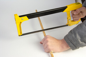 A carpenter cuts a wooden stick with a hand saw on a white background, hands and a hacksaw are...