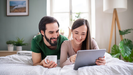 Fototapeta premium Young couple in love using tablet on bed indoors at home.