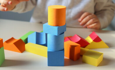 Geometric multi-colored figurines for children's games close-up and the hands of a child in the background.