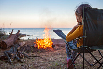 Family local getaway. Kid sitting on the touristic armchair and looking at fire before overnight at...