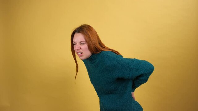 Unhealthy young woma suffering back ache, lower lumbar discomfort, painful muscle spasm, rheumatoid arthritis or pinched nerve. indoor studio shot isolated on yellow background