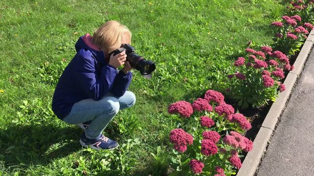 Girl photographs a butterfly on flowers while walking in the park. Child is watching nature. 