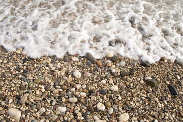 Texture. A pebble beach and the foam of the sea waves. 