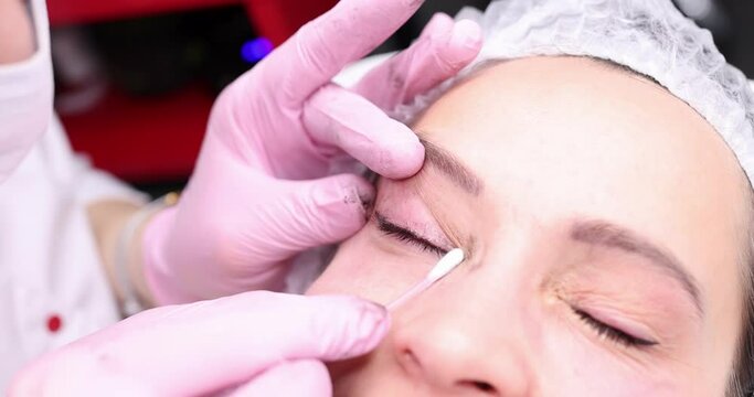 Beautician wiping clients eyelid with cotton swab 4k movie. Preparation for permanent makeup concept