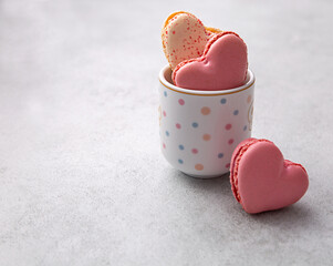 Macarons or French macaroons in heart shapes in a cup on gray background with copy space