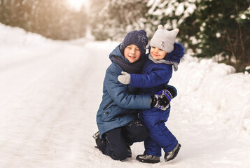 Fototapeta na wymiar Little sister hugs brother in winter in the woods on a sunny day