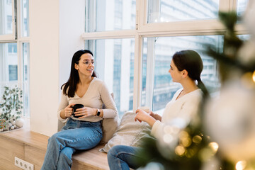 Cheerful friends sitting on window sill while talking