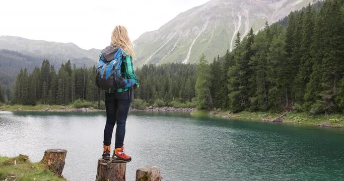 Mature adult woman solo traveler with back pack standing by lake enjoying scenic panoramic nature landscape outdoors 