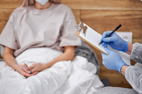 doctor asks female patient about state of health, professional doctor taking notes, covid-19. stay at home concept during Coronavirus pandemic and self isolation. focus on pen and paper, hands