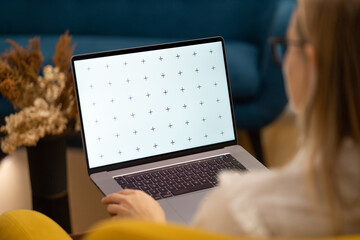 Young student girl writing essay or document on laptop. Living room working, beautiful decors, colorful interior.