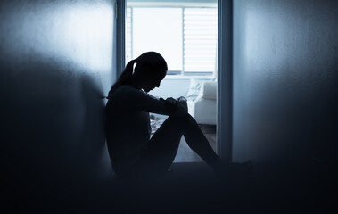 Sad lonely woman sitting on the floor at home in a dark room. People problems, and mental health...