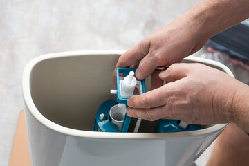 A plumber installs a water pump in a ceramic toilet cistern. Drainage system installation, home repair