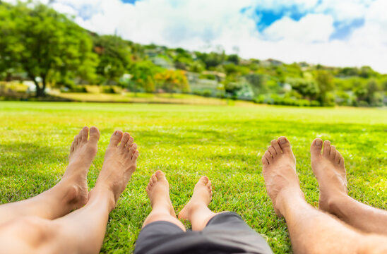 Family of three relaxing their bare feet on green grass in the country park. Parenting and family vacation getaway concept.  