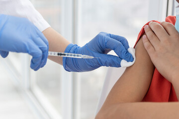 Vaccination process. Doctor's hands in medical gloves making injection with syringe  to child's arm. Preventive measures to protect from viruses.