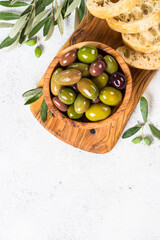 Olives in wooden bowl and ciabatta on wooden board on white background. Top view with copy space.