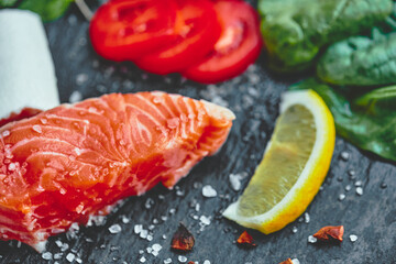 Raw salmon fillet and ingredients for cooking on a dark background.