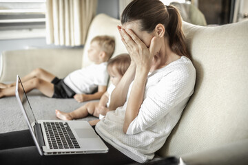 Stressed frustrated mother at home with children working on computer. 