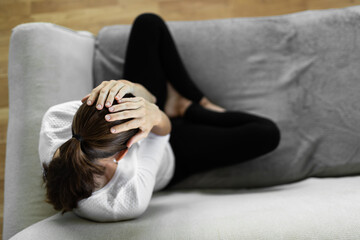 Young woman feeling sad and with hand over head sitting on couch