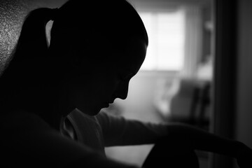 silhouette of sad woman home alone in a dark room 