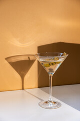 Cocktail vodka martini with green olives on orange background with bright beautiful shadows