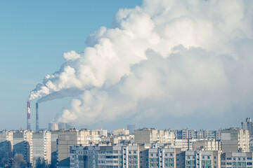 Thick white smoke from factory pipes covers city houses with smog.