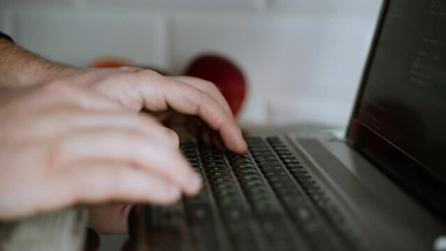 Men's hands press the keys of a laptop keyboard. A man writes a program. The developer is coding. The program code is visible on the screen. Work at home
