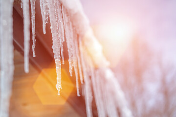 Spring bright sunlight shines on melting icicles hanging from roof