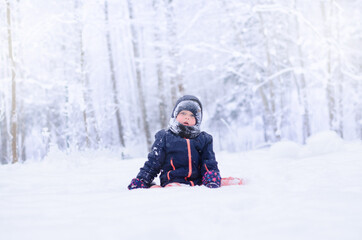 Fototapeta na wymiar little girl sitting on the snow in the winter forest