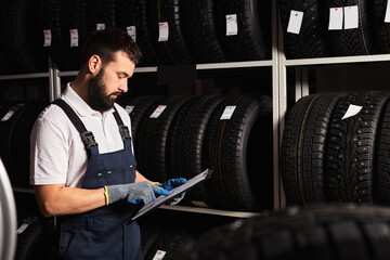 Mechanic holding paper tablet document in hands while checking the assortment in car repair service, expertise mechanic working in automobile repair garage alone, serve the customers