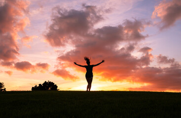 Woman feeling happy with arms up to the sunset jumping for joy.