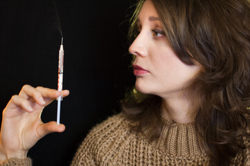 Obraz premium Vaccine concept. Female portrait of caucasian girl holding a syringe and looking at it on black background in studio.