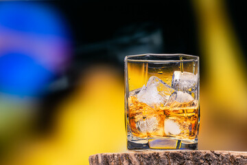 Glass of whiskey or cognac and ice cubes bright background in vintage style. Alcoholic drink with ice whiskey or cognac close-up on an oak coaster for glasses for spirits.