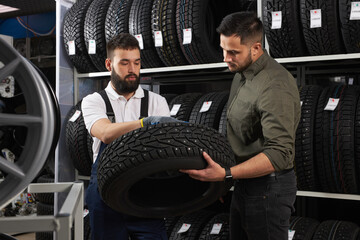 salesman of tires talking about characteristic of product to customer came to look at assortment...