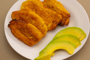 plato tipico dominicano, platanos verdes fritos acompañados de varios aguacates cortados, comida en casa, acercamiento, mesa limpia