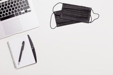 workstation with laptop, notepad, pen, black face masks, business flat lay, top view on a white background, copy space